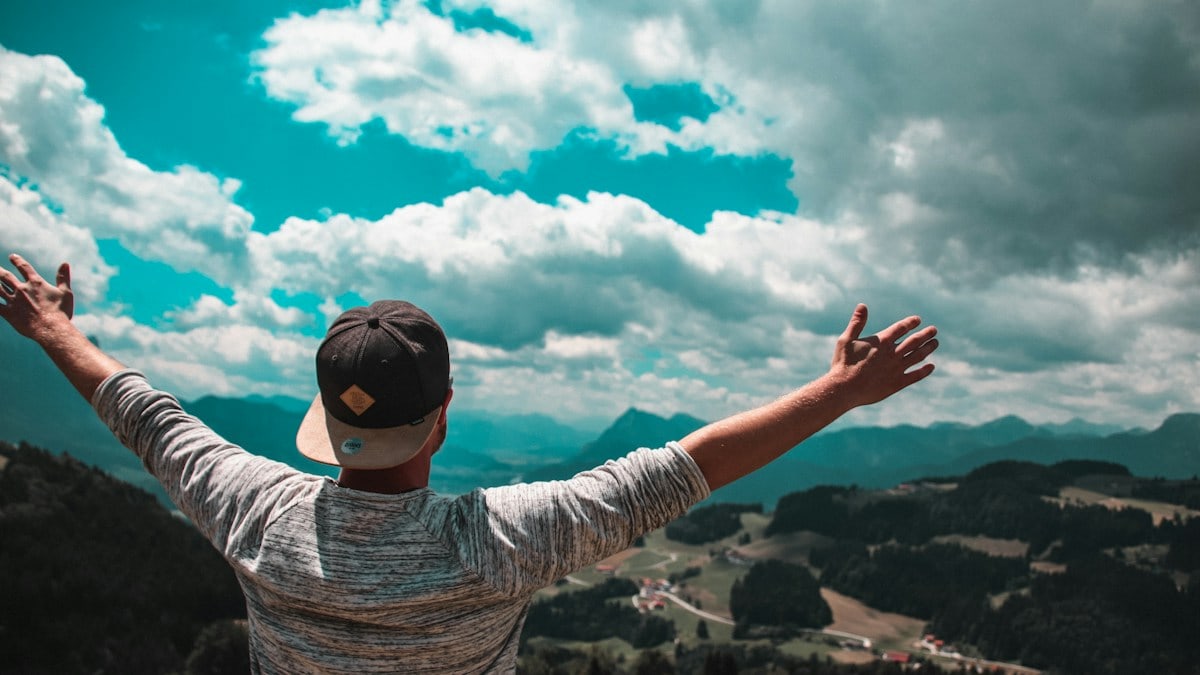 man in grey shirt with black fitted cap raising his hands